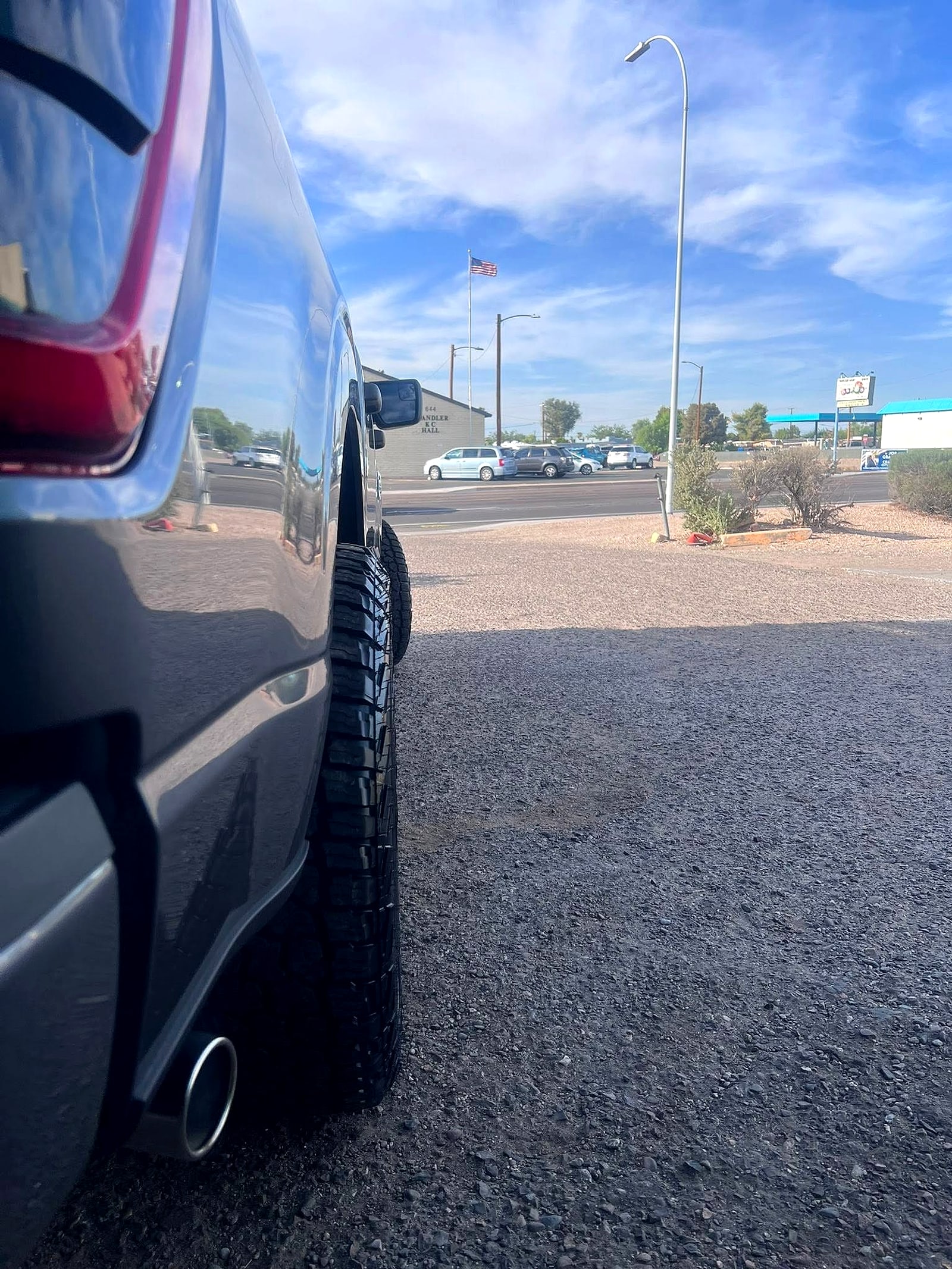 Rear tire and chrome exhaust tip of a pickup on the lot, blue Chandler sky